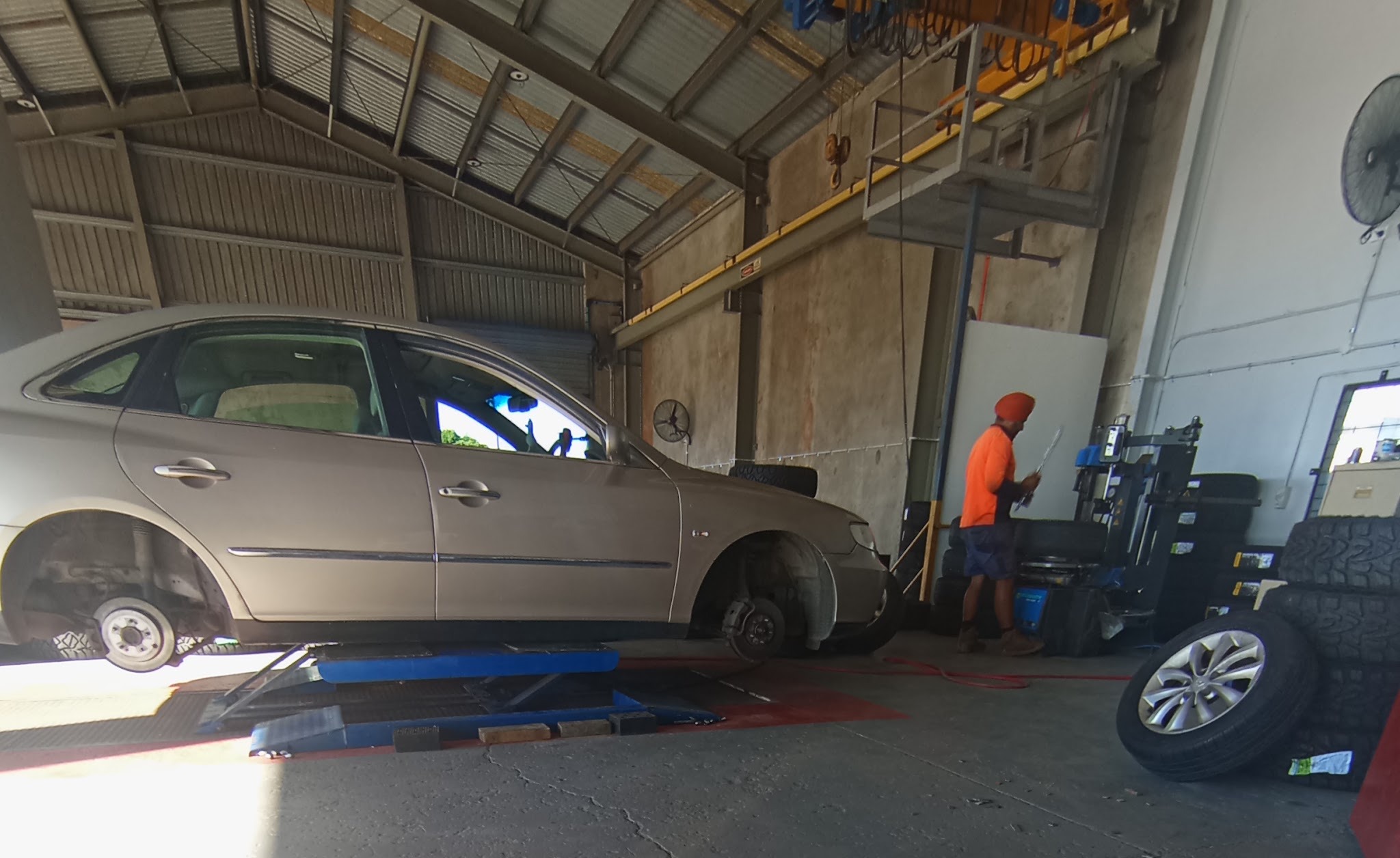 A car up on the hoist at All Budget Tyres while the owner works at the tyre machine