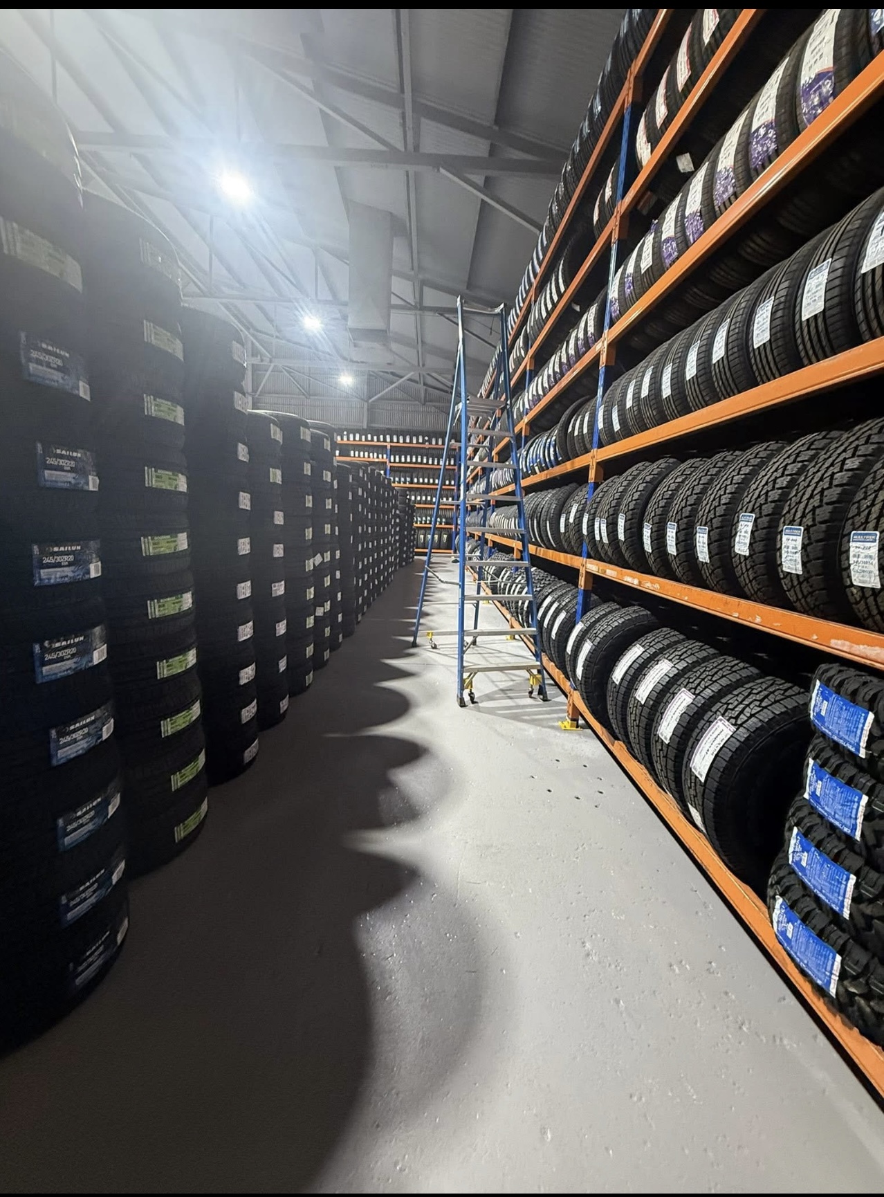 Tall shelving stacked with tyres at All Budget Tyres, with a step ladder in the aisle