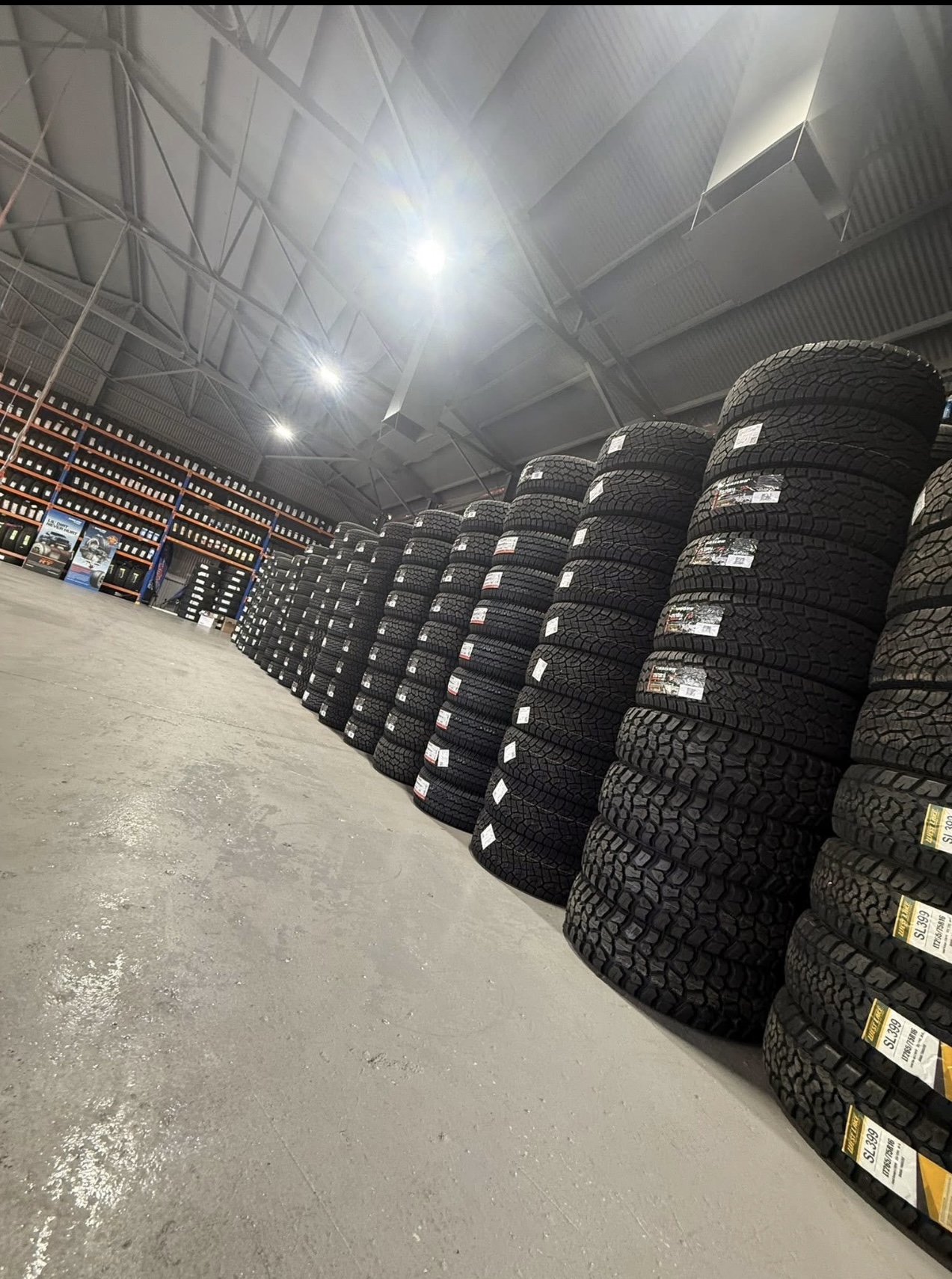 A long aisle of stacked tyres running the length of the All Budget Tyres warehouse